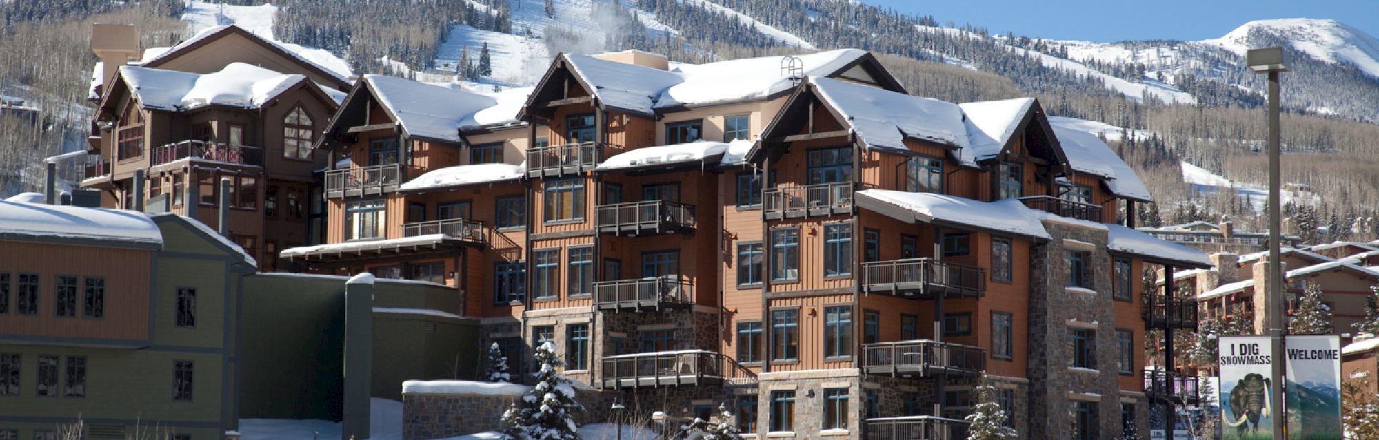 The image shows a multi-story, snow-covered building complex with surrounding mountains in the background.