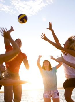 A group of people playing beach volleyball with the sun setting in the background, creating a lively and energetic atmosphere.