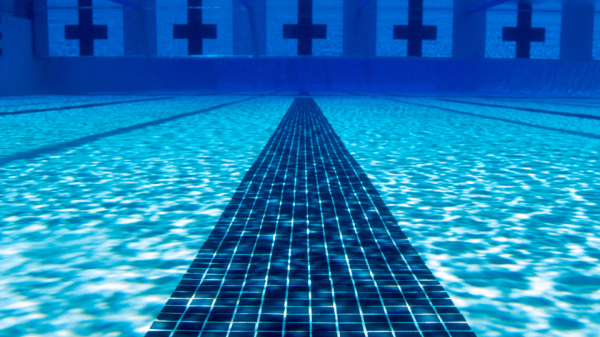 The image shows an underwater view of a clear, empty swimming pool with lane markers and a tiled floor, likely taken from one end looking towards the other.