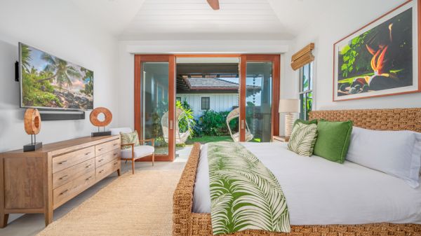 A tropical-themed bedroom with a wicker bed, green accents, large sliding glass doors, a TV, and wooden furniture leading to an outdoor area.