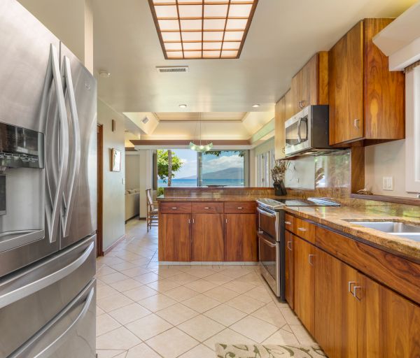 A modern kitchen with stainless steel appliances, wooden cabinetry, and a view of the ocean through large windows.