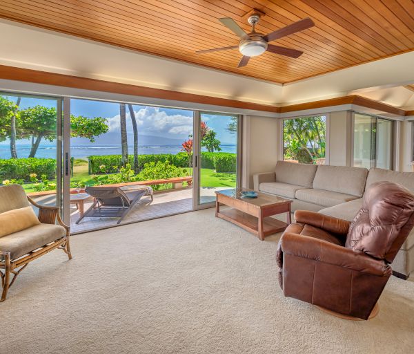 A spacious living room with a mix of modern and classic furniture, large windows offering an ocean view, and a sliding door leading to a patio.