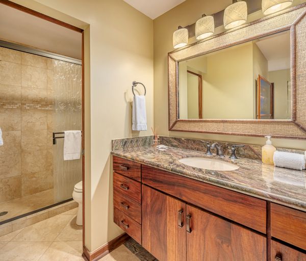 The image shows a bathroom with a glass-enclosed shower, wooden vanity, granite countertop, large mirror, and cream-colored walls.