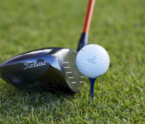 A golf club preparing to hit a golf ball on a tee placed on a grassy surface.