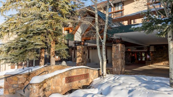 A snow-covered entrance to a building surrounded by trees, featuring a sign that reads "Stonebridge Lodge."