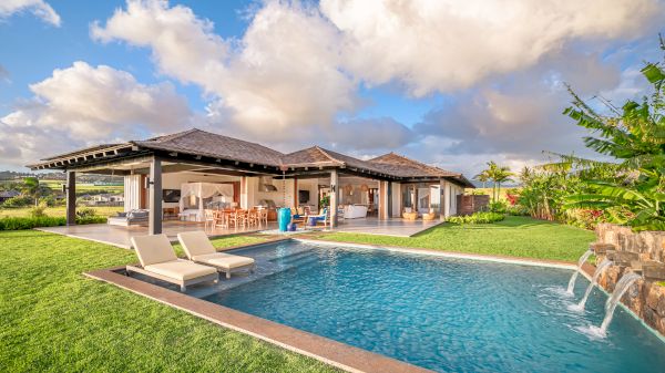 The image shows a luxurious villa with an outdoor pool, lounge chairs, and a beautiful garden, set against a backdrop of cloudy sky and lush greenery.