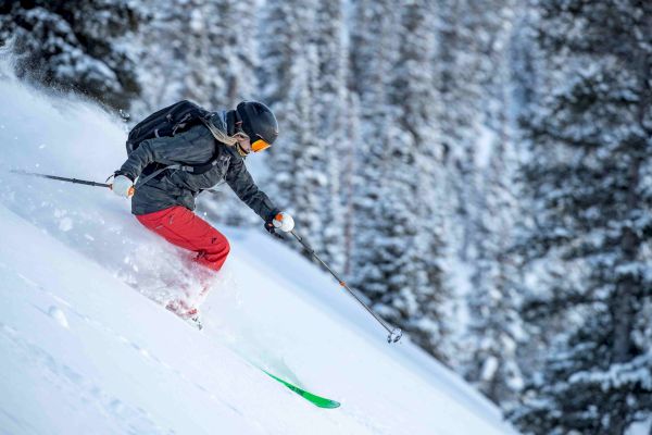 A skier in a black helmet and red pants is descending a snowy slope with skis, surrounded by snow-covered trees in the background.